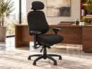 A black fabric ergonomic office chair with a headrest, adjustable armrests, and a five-wheel base, positioned in front of a wooden desk in a modern office setting.